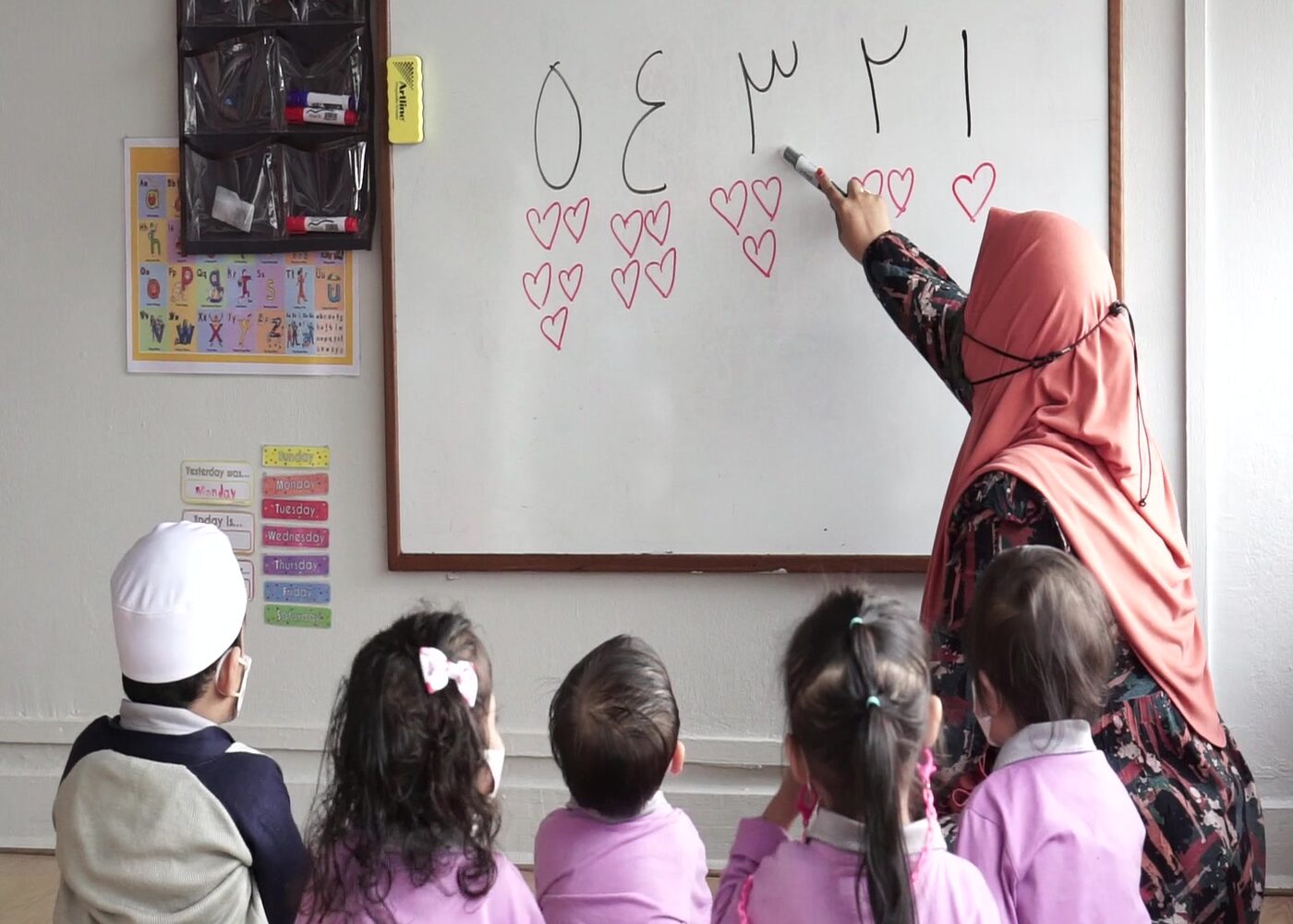 A teacher writing Arabic numerals on the board at Kidya Childcare